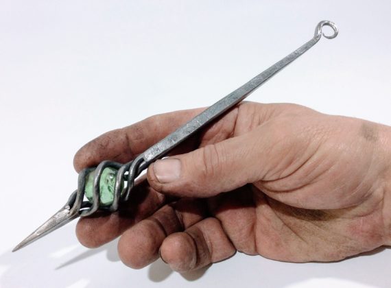 hand forged steel oddment approximately the length of a pen, incorporating a glass marble held in a twisted steel cage